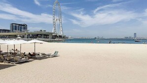 Een strand met ligbedden en parasols, een groot reuzenrad en uitzicht op de oceaan en verre gebouwen.