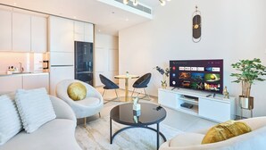 Een moderne woonkamer met een flatscreen televisie, twee fauteuils, een bank en een eethoek.
