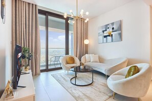 A modern living room with a sofa, armchair, coffee table, and a TV on a stand. - 5-Star Address Beach Resort | 1BR High Floor (Dubai)