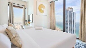 Hotelkamer met een groot bed, een bureau, een stoel, een vaas met bloemen, een schilderij en uitzicht op een gebouw en strand.