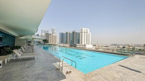 A rooftop pool with lounge chairs and a view of high-rise buildings. - Modern Chic Studio Featuring Skyline Views (Dubai)