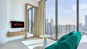 A modern living room with a large window, a flat-screen TV, and a green sofa. - Modern Chic Studio Featuring Skyline Views (Dubai)