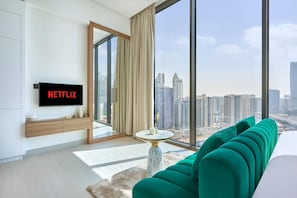 A modern living room with a large window, a flat-screen TV, and a green sofa. - Modern Chic Studio Featuring Skyline Views (Dubai)