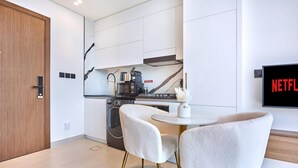 A modern kitchen with a coffee machine, a washing machine, and a dining area with two chairs. - Modern Chic Studio Featuring Skyline Views (Dubai)