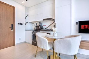 A modern kitchen with a coffee machine, a washing machine, and a dining area with two chairs. - Modern Chic Studio Featuring Skyline Views (Dubai)