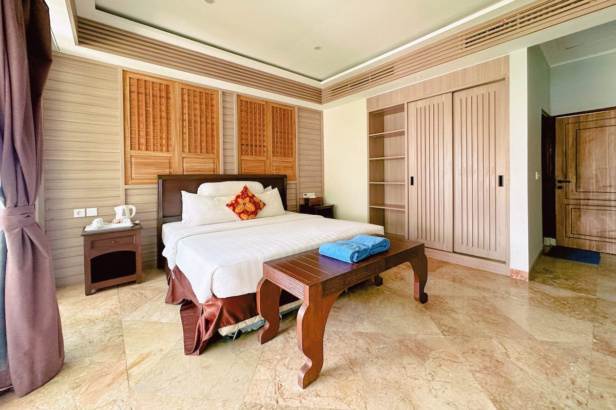 Habitación de hotel con cama, mesitas de noche, un banco de madera, armario y puerta de baño.