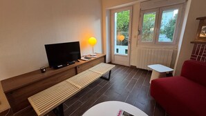 A modern living room with a flat-screen TV, a bench, a red sofa, a small white table, and a yellow lamp.