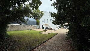 A white building with a sloped roof, a gravel pathway, and a grassy area with a decorative planter.