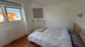 A bedroom with a window, radiator, bed, and a wall-mounted shelf.