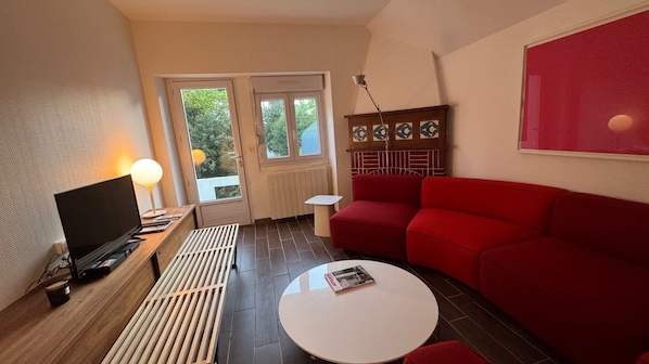 A modern living room with a red sofa, a white coffee table, a TV, and a radiator.