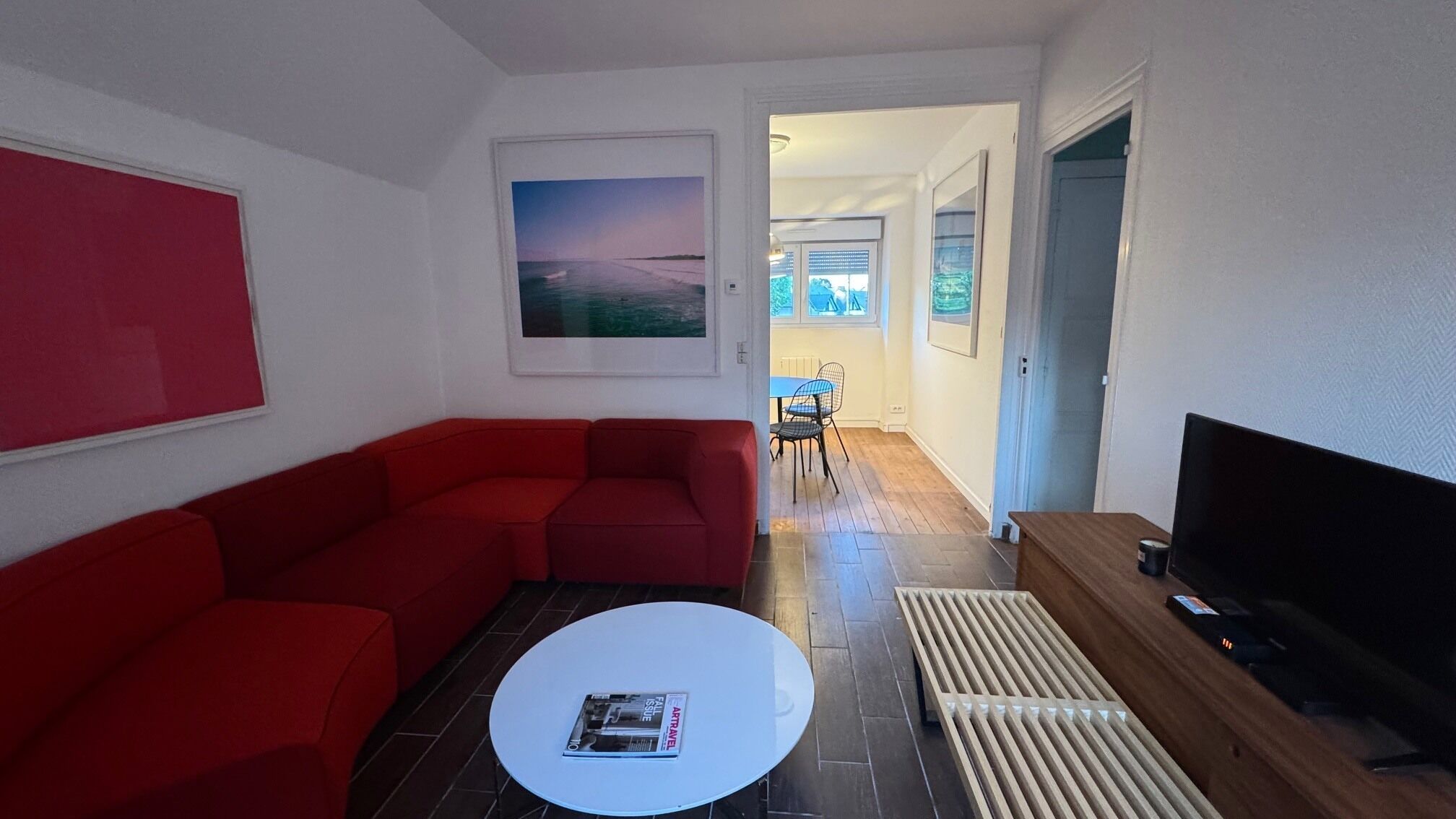 Ein Wohnzimmer mit einem roten Sofa, einem weißen Couchtisch, einem Fernseher und einem Bild an der Wand.