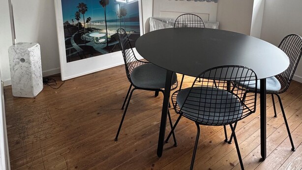A dining area with a round table, four chairs, a single pendant light, and a framed picture on the wall.