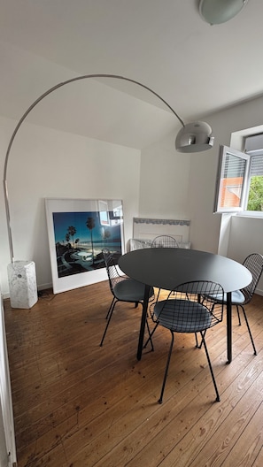 A dining area with a round table, four chairs, a single pendant light, and a framed picture on the wall.