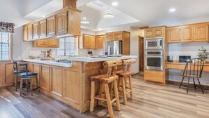 Una cucina moderna con mobili in legno, un'isola grande con sgabelli, elettrodomestici in acciaio inossidabile e un soffitto alto con illuminazione a incasso.