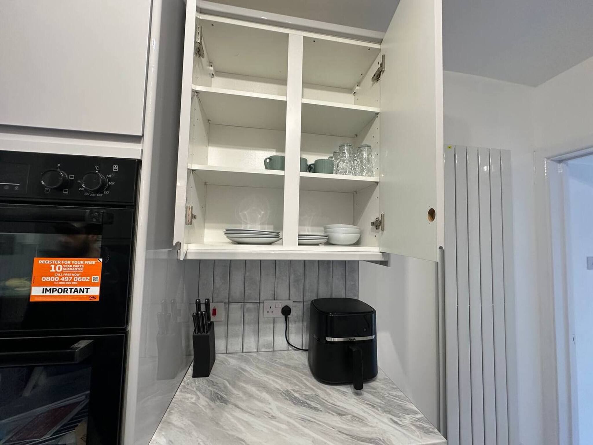 A kitchen with a built-in oven, a coffee maker, and a cabinet with dishes.