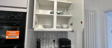 A kitchen with a built-in oven, a coffee maker, and a cabinet with dishes.