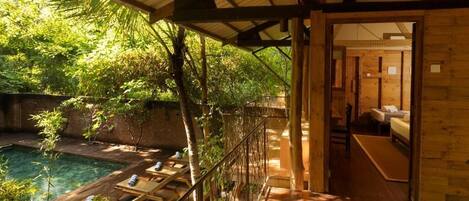 Una terraza de madera con piscina, un espacio cubierto con vistas a la vegetación y una habitación con cama y escritorio.