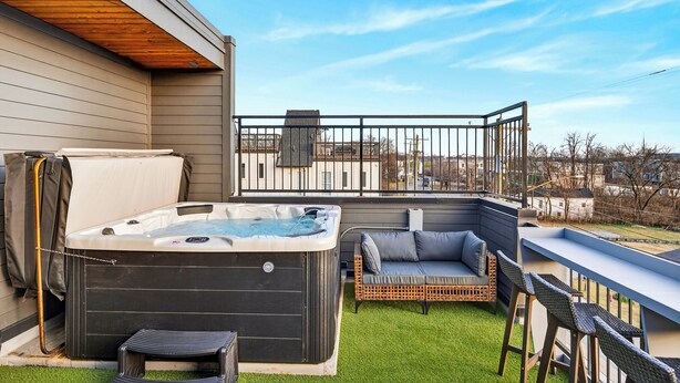A hot tub on a balcony with a view of the city, a sofa, and a railing. - 2 Homes | Hot Tub + Karaoke Lounge + Rooftop + Skyline Views | Min to Broadway (Nashville)