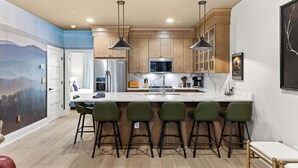 A modern kitchen with a large island, bar stools, and wooden cabinets. - 2 Homes | Hot Tub + Karaoke Lounge + Rooftop + Skyline Views | Min to Broadway (Nashville)