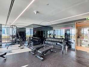 Une salle de sport moderne équipée de matériel de musculation, de bancs et d’un mur recouvert de miroirs.