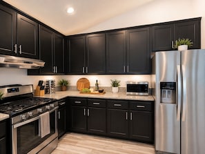 A modern kitchen with dark cabinets, stainless steel appliances, and a granite countertop. - Skyline Hilltop 6BR Villa | Best Views in SD (Spring Valley)