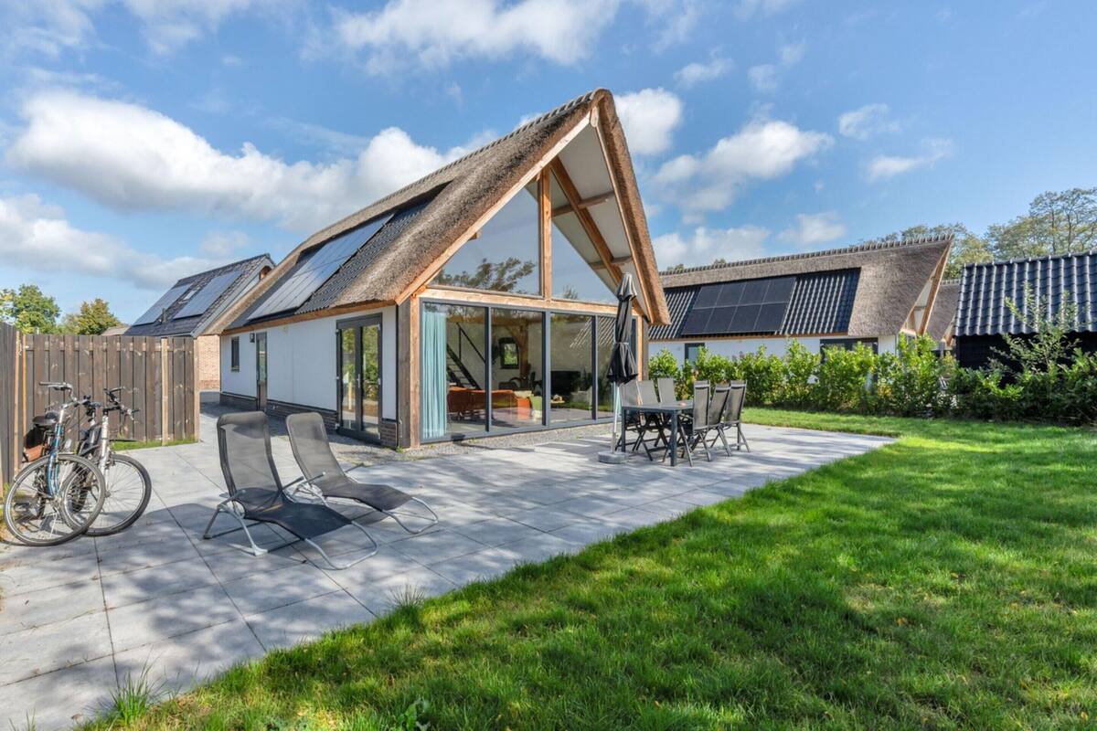 A modern house with a sloped roof, solar panels, a patio with chairs and a table, and a bicycle.