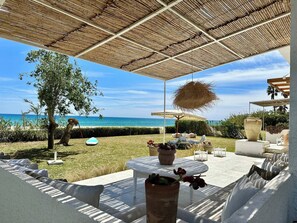 An outdoor patio with a view of the ocean, covered by a thatched roof, and furnished with white chairs and tables. - Beach House Hammamet (Mrezga)
