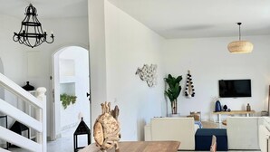 Una sala moderna con una mesa de comedor de madera, muebles de mimbre y un televisor grande.