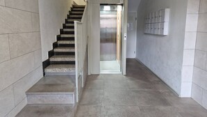 A hallway with a staircase leading to an elevator, tiled walls, and a row of lockers on the right. - 114m² 3 Bedroom Apartment with Balcony Lift and AC (Nules)