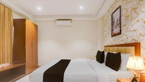 A hotel room with a bed, bedside table, lamp, air conditioning unit, wardrobe, and a framed picture on the wall.