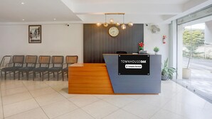 A reception desk with a clock, a framed picture, and a row of chairs.