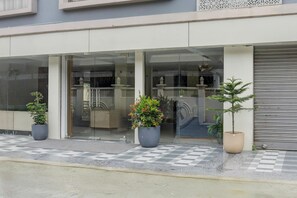 Un bâtiment à la façade moderne, doté de grandes fenêtres en verre et orné de plantes en pot devant l’entrée.