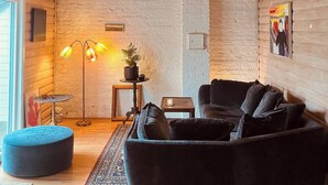 Ein gemütliches Zimmer mit einem dunklen Sofa, einem runden Hocker, einer Stehlampe und einer Pendelleuchte.