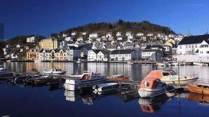 Ein Hafen mit Booten, eine Stadt mit Häusern und eine Hügelkette im Hintergrund.