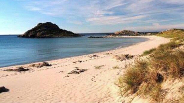 Ein Strand mit sandigem Ufer, einem kleinen Hügel und einem klaren Himmel.