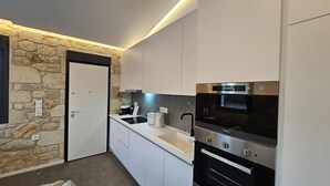 Une cuisine compacte avec un mur d’accent en pierre, un four encastré et une machine à café.