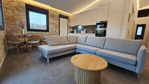 Un salon moderne avec un canapé d’angle gris, une table basse ronde en bois et un mur décoratif en pierre.