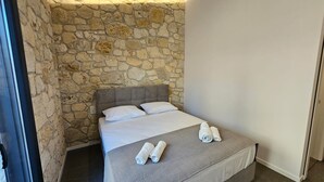 Un lit simple avec une tête de lit grise, du linge de lit blanc et deux serviettes enroulées posées sur le lit.