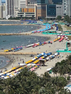 A beach with rows of umbrellas and people, a rocky breakwater, and buildings in the background. - El Laguito Beach Cartagena (Cartagena)