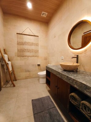 Une salle de bain moderne avec un plafond en bois, un miroir rond, un lavabo beige et des toilettes.