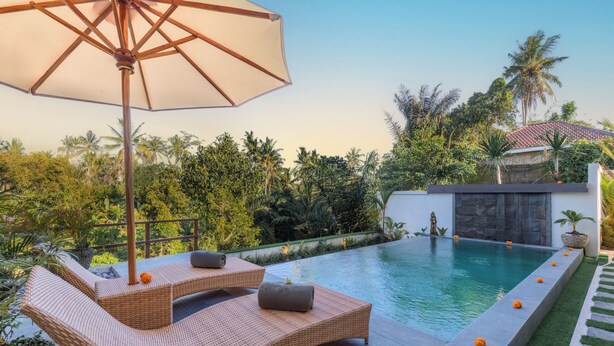 Ein Poolbereich mit Liegestühlen, Sonnenschirm und Blick auf den Pool und die umliegende Bepflanzung.