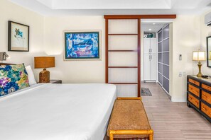 Hotellihuone, jossa on sänky, penkki, yöpöytä, lamppu, taulu ja vaatekaappi.