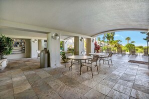 A covered patio area with stone flooring, outdoor seating, and a view of a tropical landscape. - The Palms at Wailea 1805 - Luxury 2BR condo, large lanai, Full AC, Kitchen, WiFi (Kihei)