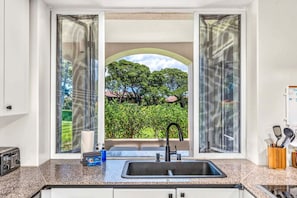 A kitchen with a built-in sink, a toaster, and a window with a view of greenery and trees. - The Palms at Wailea 1805 - Luxury 2BR condo, large lanai, Full AC, Kitchen, WiFi (Kihei)