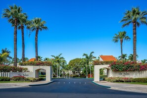 A gated entrance with palm trees, a clear blue sky, and a sign reading 'The Palms.' - The Palms at Wailea 1805 - Luxury 2BR condo, large lanai, Full AC, Kitchen, WiFi (Kihei)