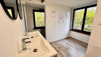 Une salle de bain moderne avec un grand lavabo, deux miroirs, une fenêtre et une porte donnant sur une autre pièce.