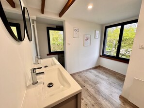 A modern bathroom with a large sink, two mirrors, a window, and a door leading to another room. - The Campagnarde (Flers)