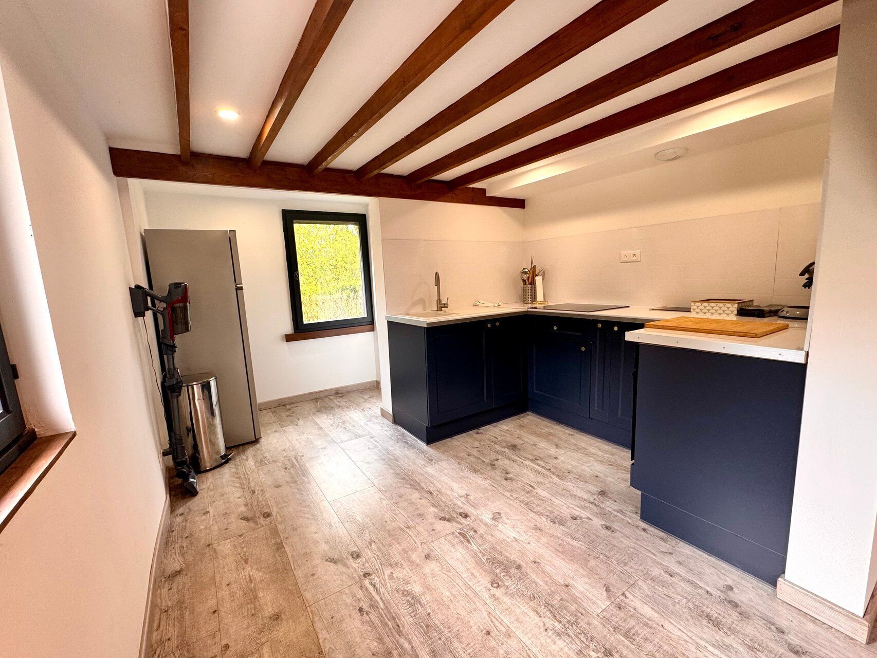 A modern kitchen with dark cabinets, a wooden floor, and a window with a view of greenery.