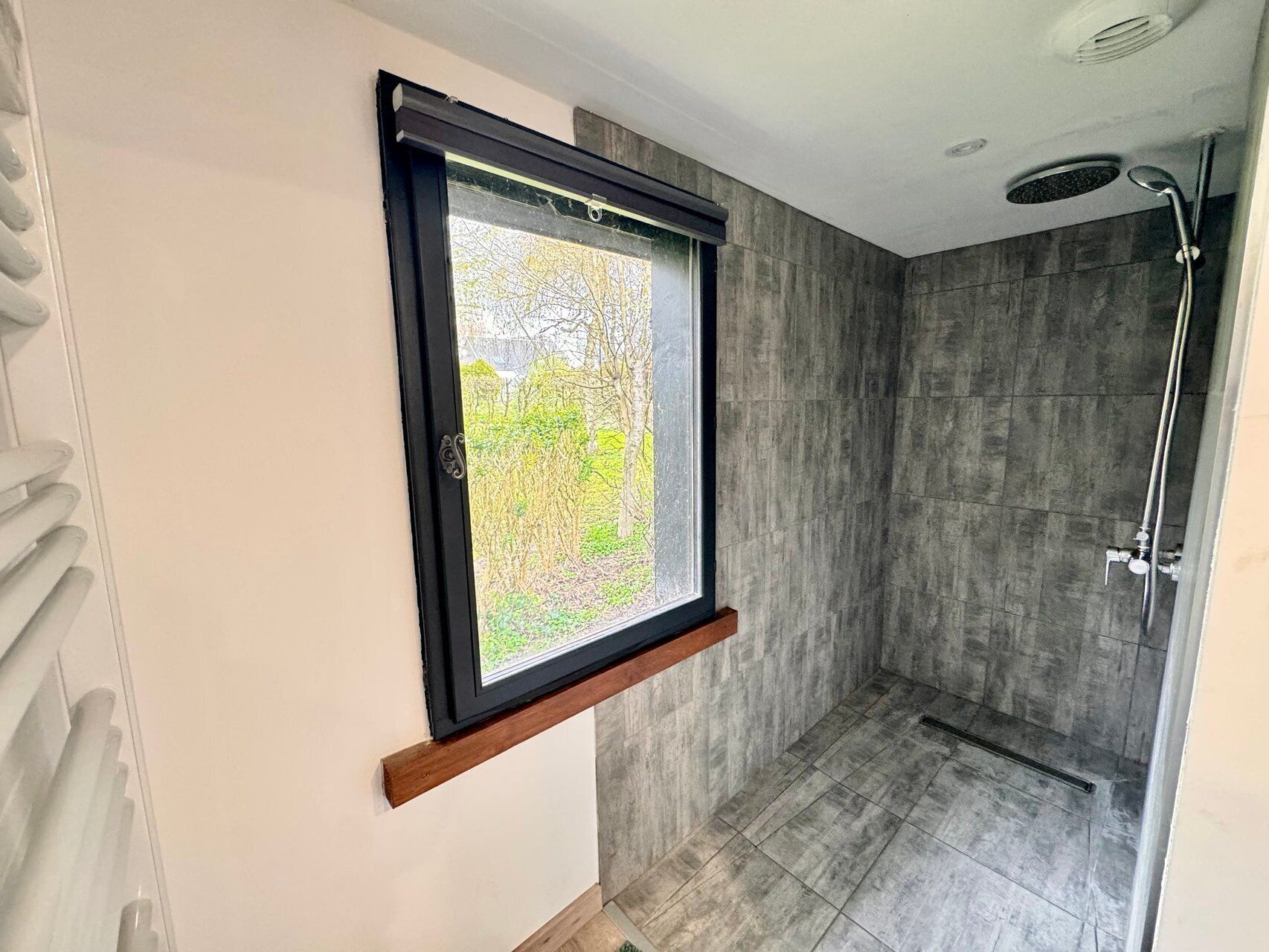 Ein Badezimmer mit Fenster, Dusche und Blick auf Bäume.