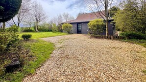 A house with a gravel driveway, surrounded by trees and a grassy area. - The Campagnarde (Flers)